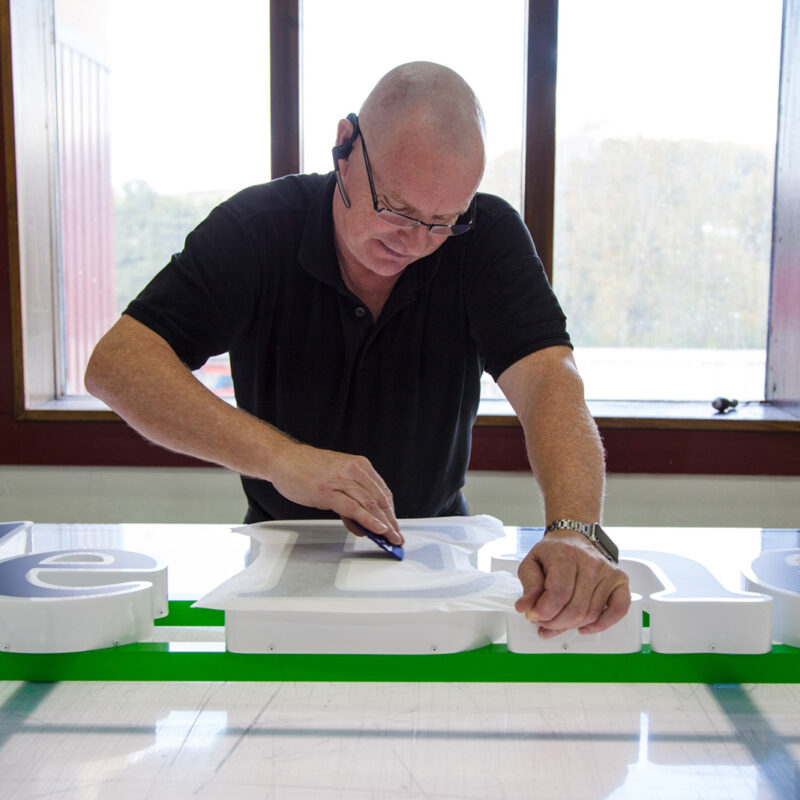 Montör på skyltfabriken applicerar en svart blockout folie på en fasadskylt med innerbelyst LED.