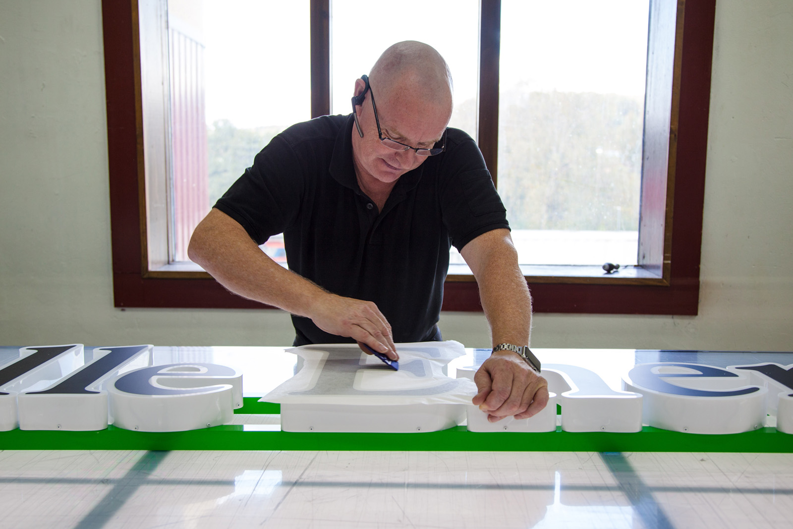 Montör på skyltfabriken applicerar en svart blockout folie på en fasadskylt med innerbelyst LED.