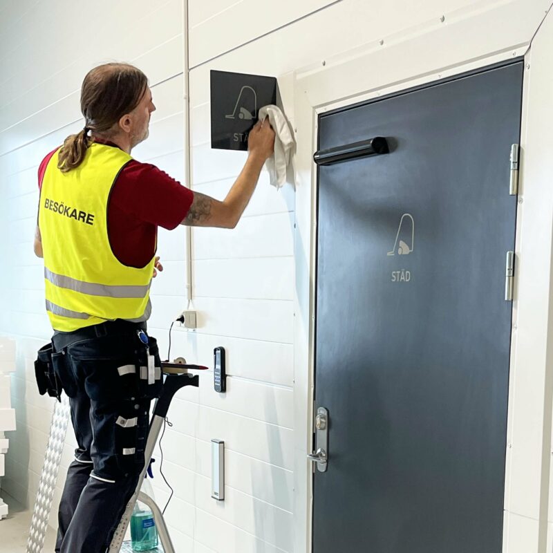 En skyltmontör står på en stege och torkar av en interiör flaggskylt med en putsduk.