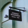 Dubbelsidig obelyst flaggskylt. Tillverkad av aluminium, nedpendlad från stag/fäste.