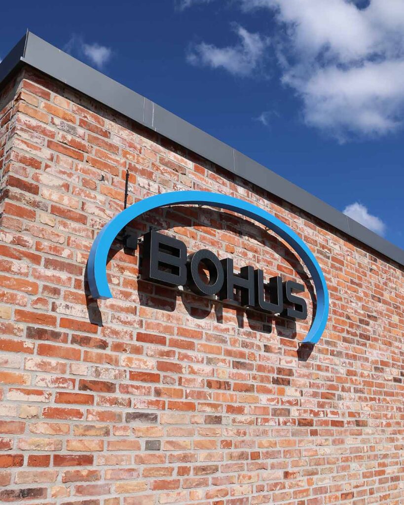 Fasadskylt för Bohus ombyggda fastighet på Exportgatan, Hisings Backa. Blå och svart fasadskylt där de svarta tecknen lyser med vit ljuseffekt på natten.